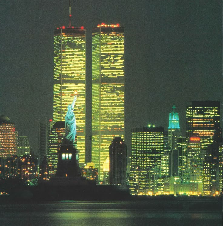 the statue of liberty is lit up at night in front of the new york city skyline