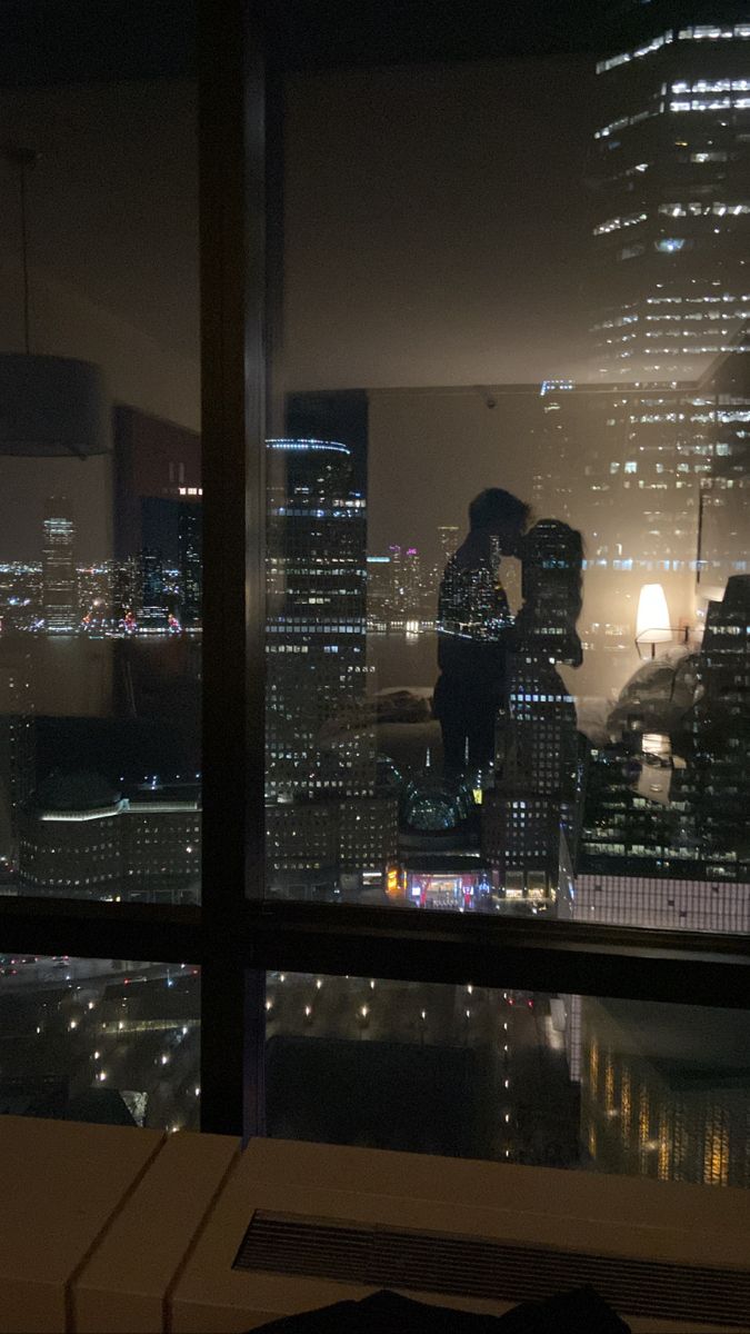 two people standing on top of a building at night with city lights in the background