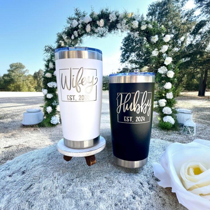 two personalized tumblers sitting on top of a rock next to a white rose