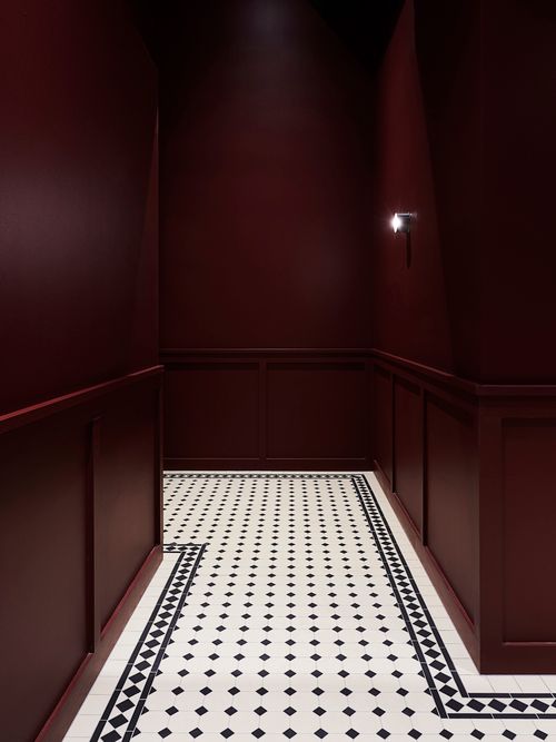 an empty room with red walls and black and white floor tiles on the floor is lit by a spot light