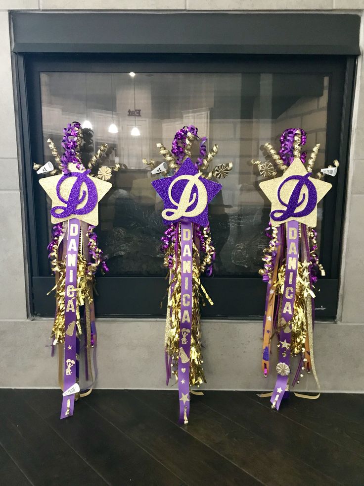 three purple and gold ribbons with the letter d on them in front of a fireplace