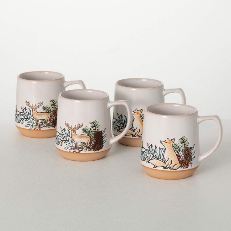 four white coffee mugs with deer and pine branches painted on the sides, sitting next to each other