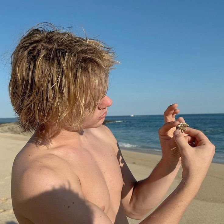 a shirtless man on the beach holding something in his hand