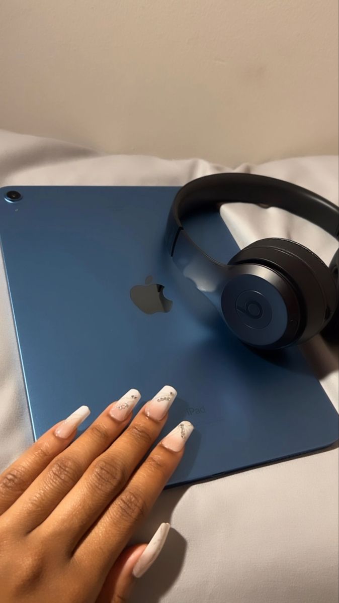 a woman's hands with french manies and headphones on top of an apple laptop