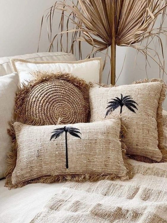 three pillows with palm trees on them sitting on top of a bed next to a plant