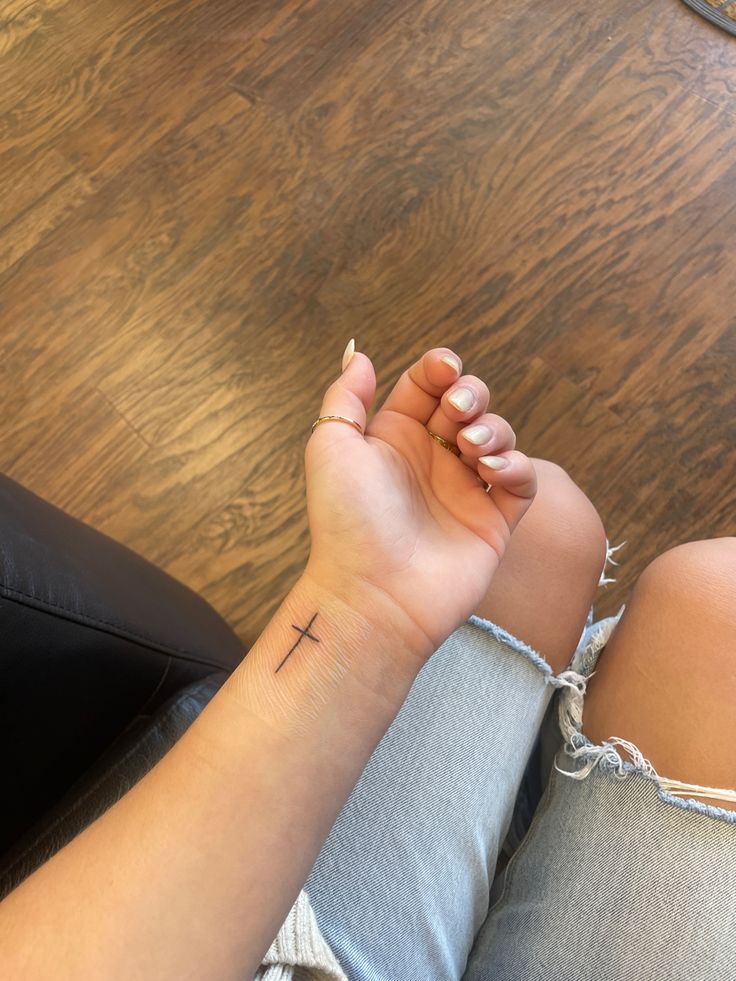 a woman with a small cross tattoo on her left wrist sitting on the floor next to a chair