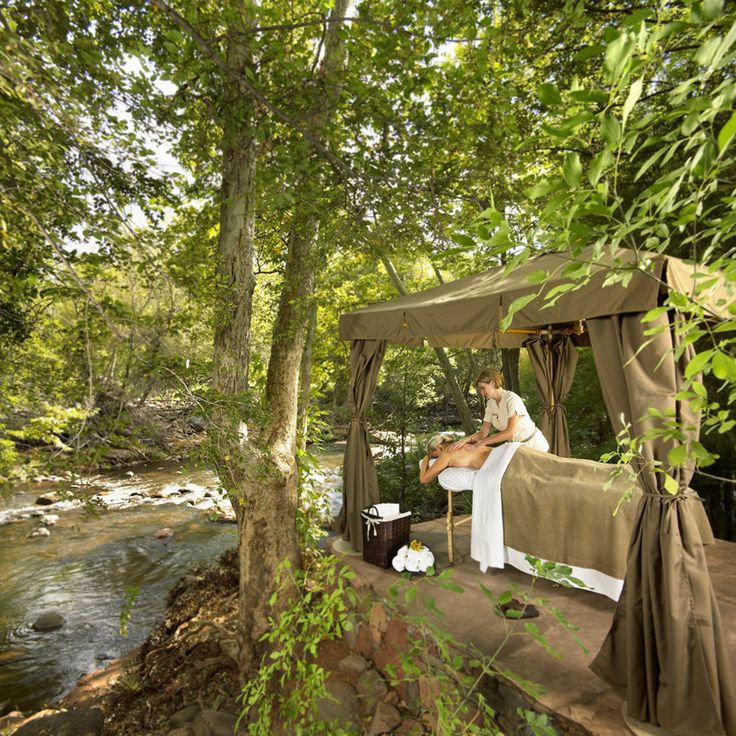 a man sitting on top of a bed under a canopy next to a river in the forest