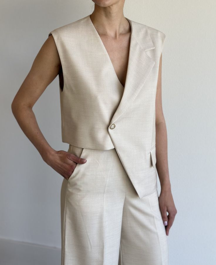 Midweight woven fabric. Boxy fit . Notch lapels. Sleeveless Asymmetric hem. Front flap pockets. Single front button closure  Lined 86% Polyester 12% Linen 2% Elastane ONE SIZE  Shoulder 15cm / 5.9in Bust 108cm / 42.5in Length 63cm / 24.8in Sleeveless Summer Vest For Tailoring, Chic Vest With Pockets, Tailored Beige Vest For Business Casual, Sleeveless Beige Outerwear For Work, Chic Asymmetrical Vest For Spring, Beige Notch Lapel Vest For Spring, Beige Vest For Work, Chic Asymmetrical Vest For Work, Beige Sleeveless Outerwear For Work