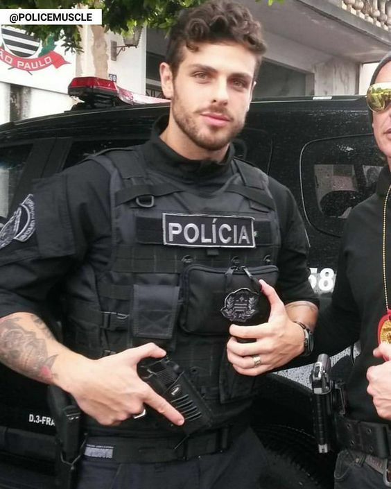 two men standing next to each other in front of a police car with their thumbs up