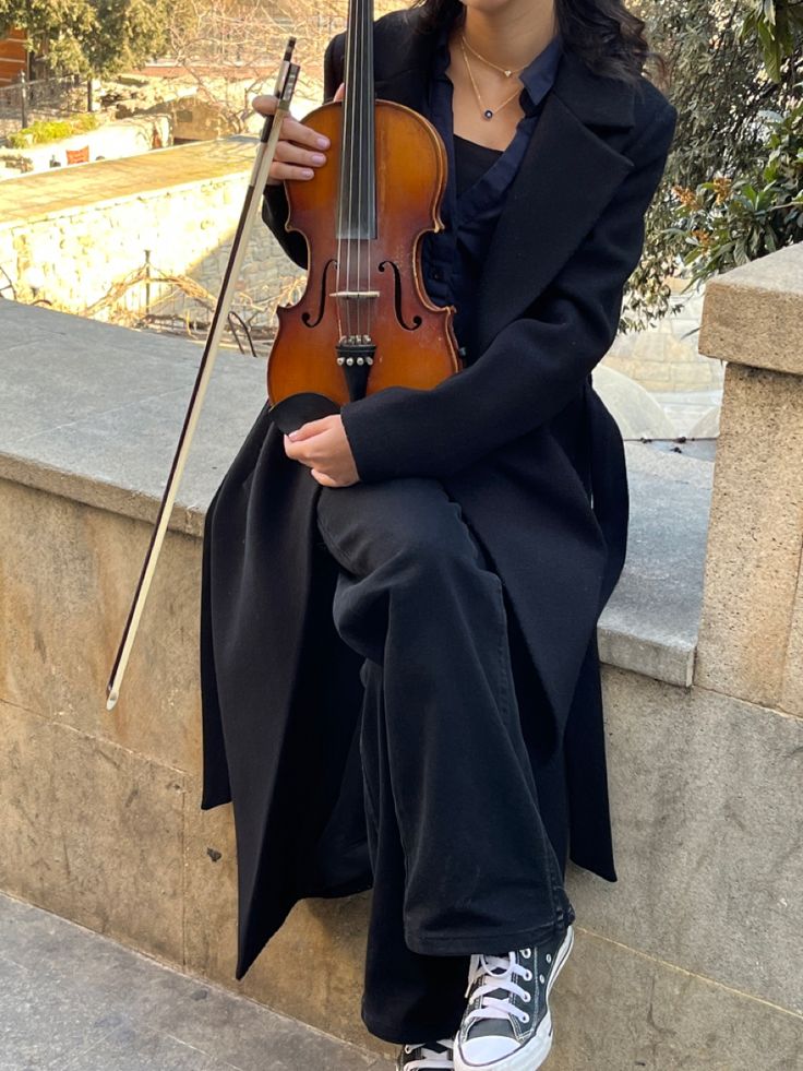 a woman holding an umbrella while sitting on the ground with a violin in her hand