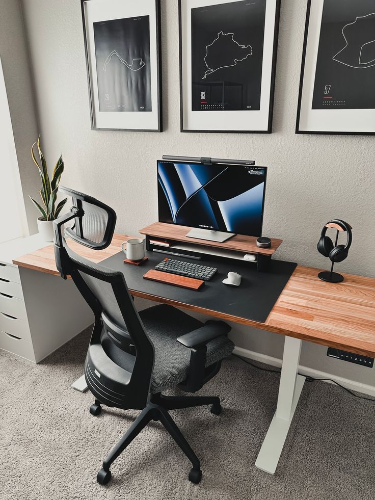 a desk with a computer on it in front of two framed pictures and a potted plant