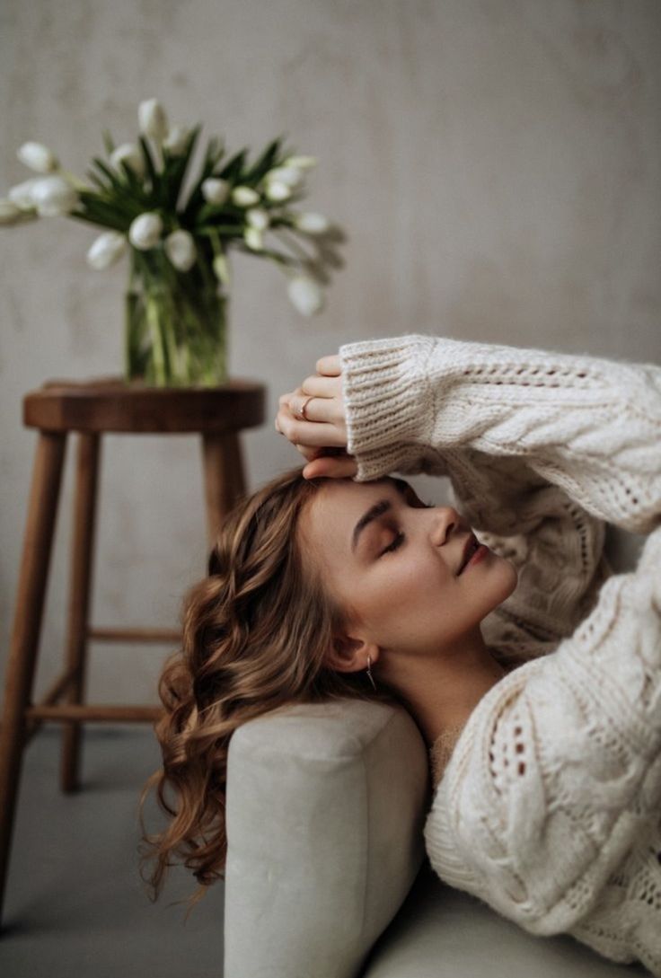 a woman laying on top of a couch next to a vase with flowers