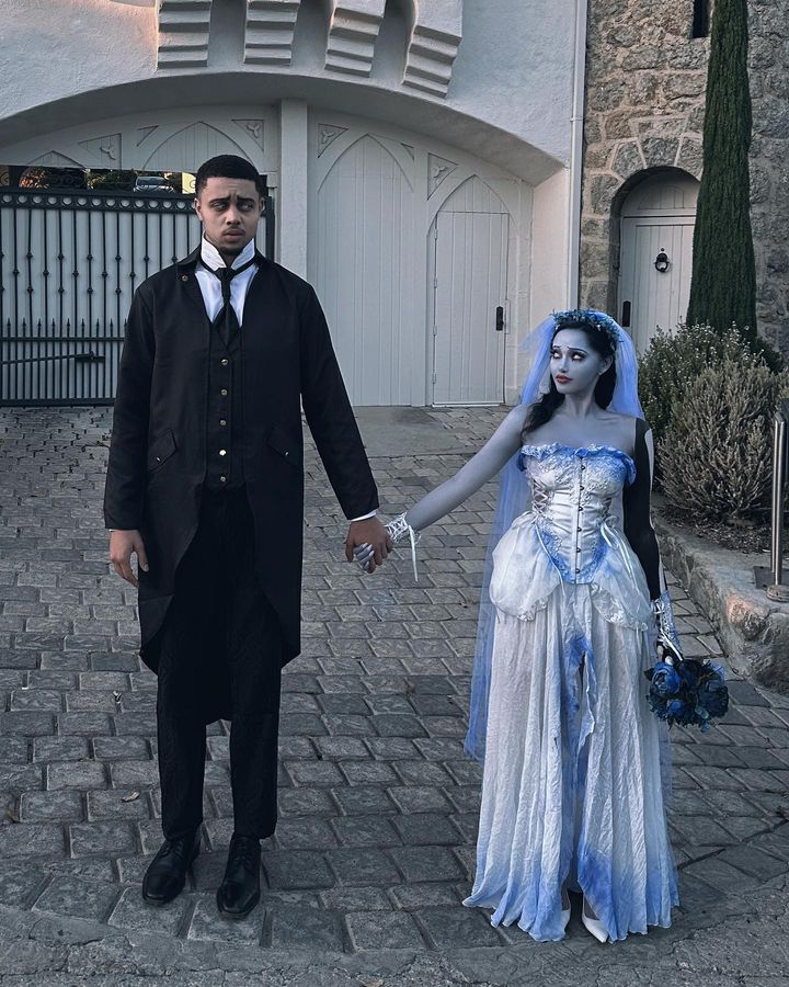 a man and woman dressed up as corpse brides holding hands in front of a castle