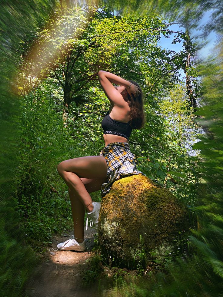 a woman sitting on top of a rock in the middle of a lush green forest