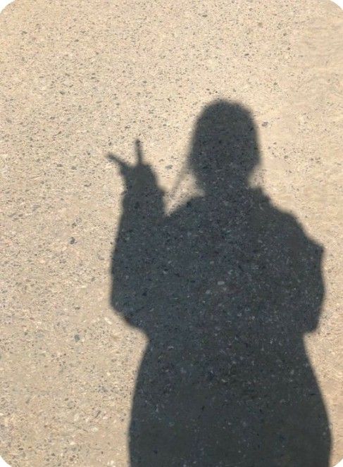 the shadow of a person holding a cell phone in their hand and pointing at it