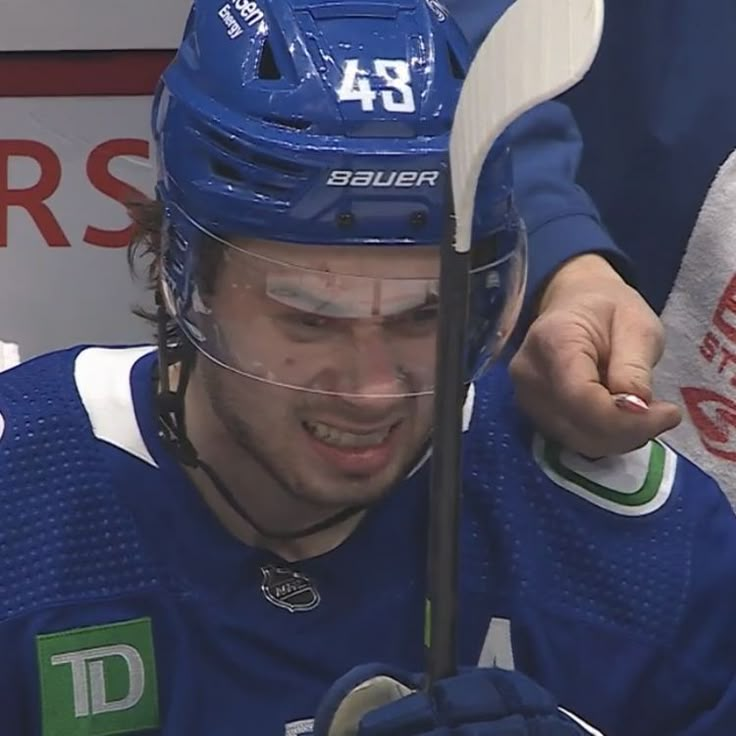 a close up of a hockey player wearing a blue uniform and holding a white stick