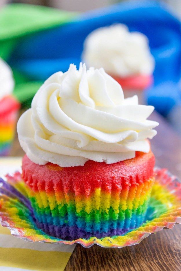 a cupcake with white frosting and rainbow icing on a colorful paper plate