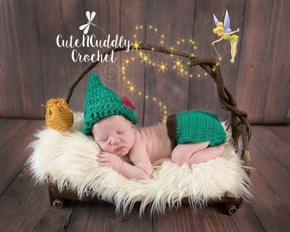 a baby sleeping in a basket wearing a green knitted elf hat and diaper