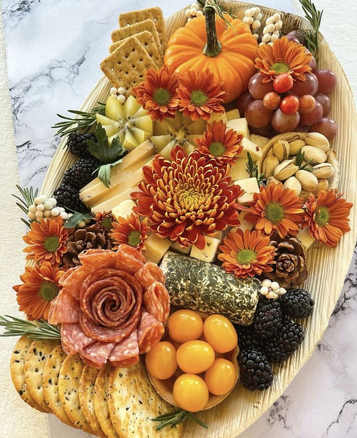 a platter filled with cheese, crackers, fruit and flowers on top of a marble counter