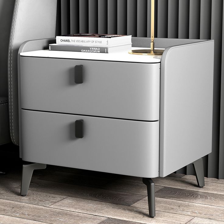 a nightstand with two drawers and a lamp on top of it next to a chair