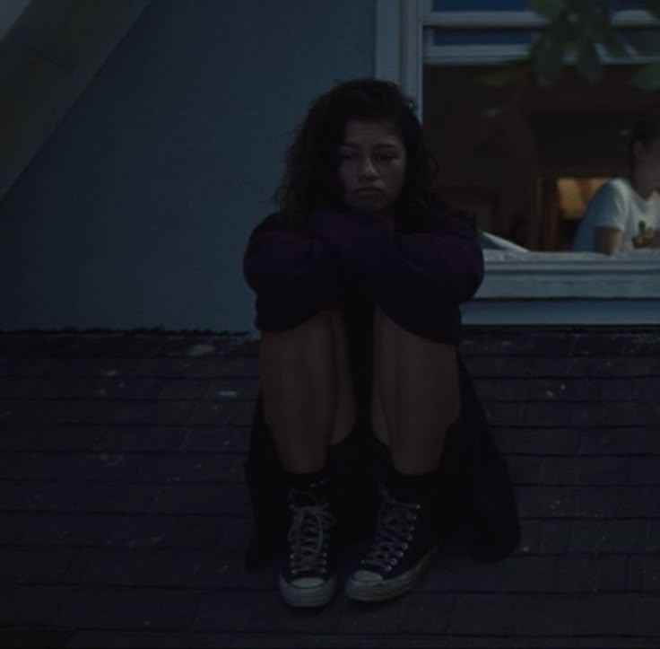 a woman sitting on the ground in front of a window with her legs crossed and head down