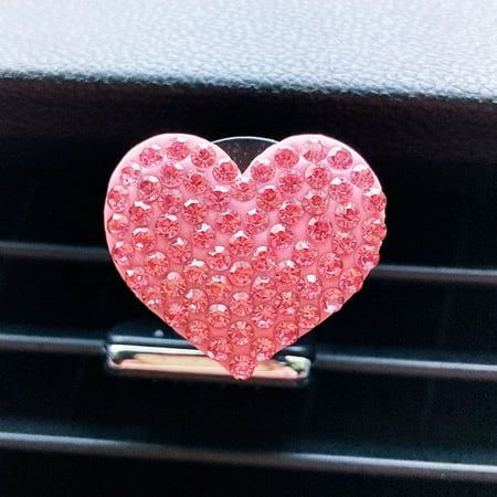 a pink heart shaped brooch sitting on top of a car dash board in front of a steering wheel