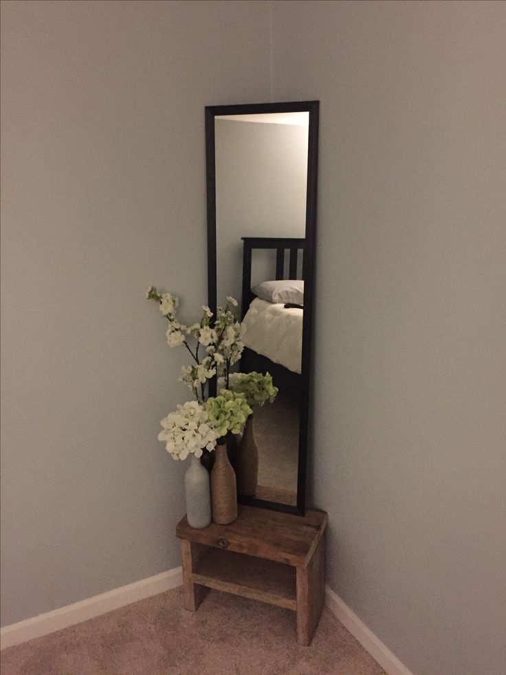 a vase with flowers sitting next to a mirror on the wall in a room that is painted light blue