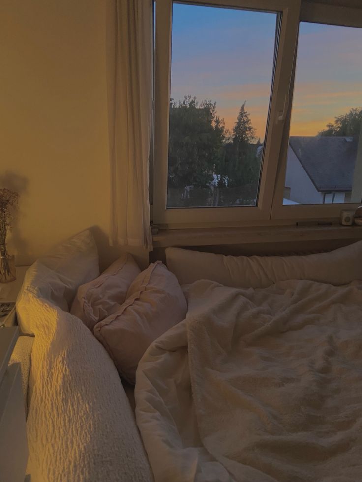 an unmade bed sitting in front of a window with the sun setting on it