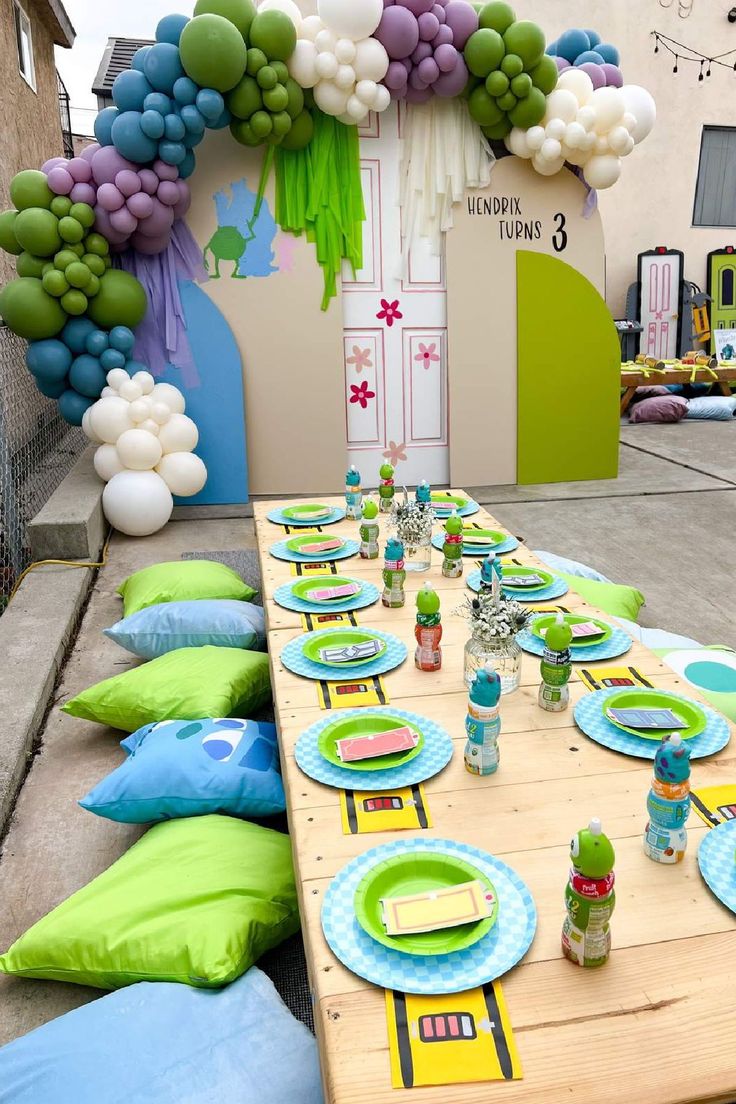 a long table set up for a party with balloons and decorations on the wall behind it