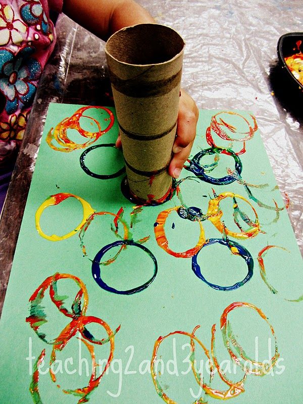 a child's hand holding a paper cup over a painting with rings on it