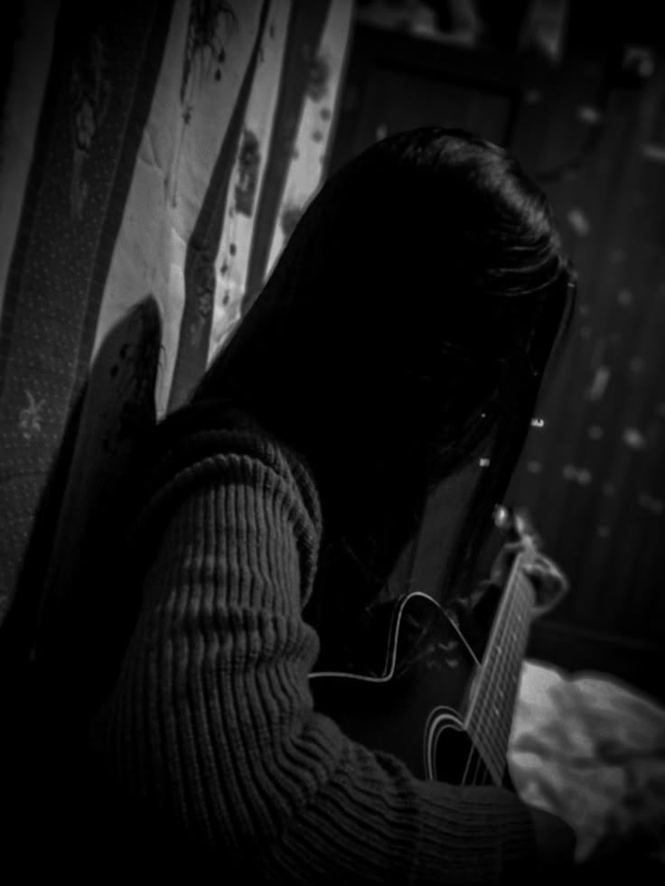 black and white photograph of a person playing an acoustic guitar in a dark room with striped wallpaper