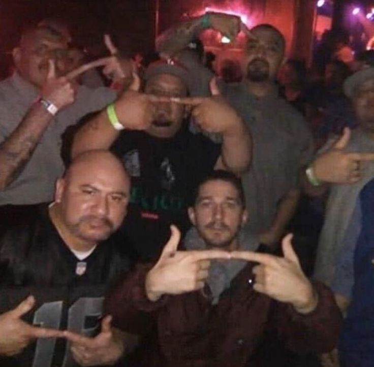 a group of men standing next to each other at a bar with their fingers in the air