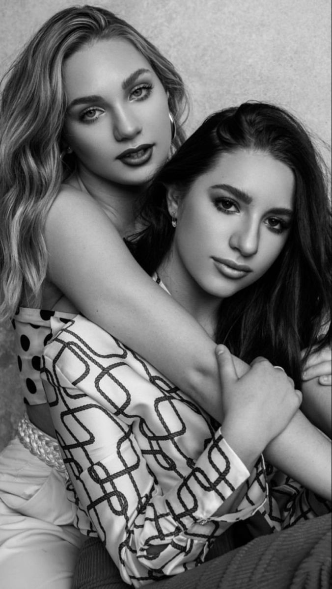 two beautiful young women sitting next to each other on top of a bed in black and white