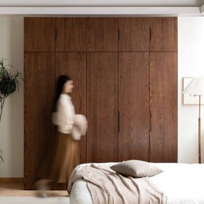 a woman walking past a bed in a room with white walls and wood paneling