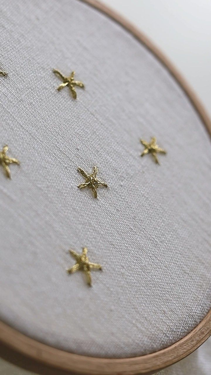 a close up of a cross stitch pattern on a white cloth with some gold stars