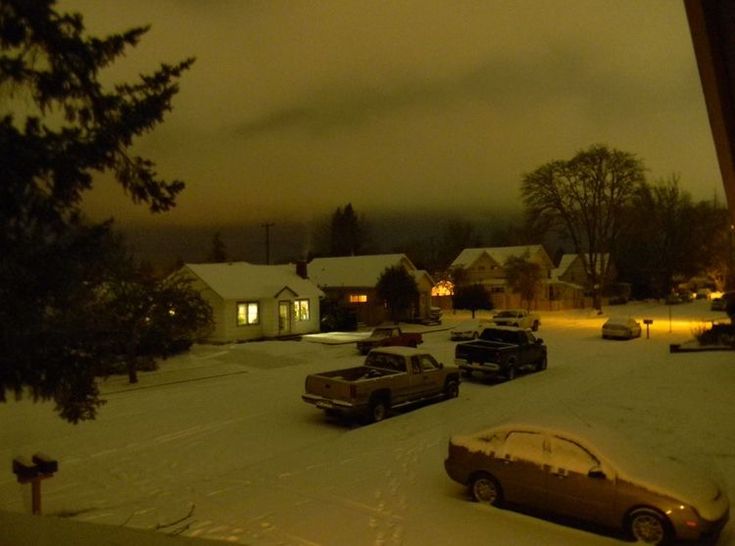 cars are parked on the snow covered street in front of some houses at night time