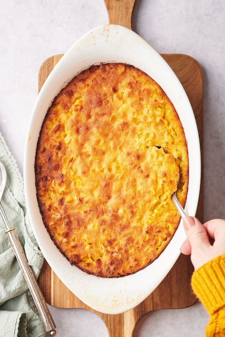 a baked dish in a white bowl on top of a cutting board next to a knife and fork