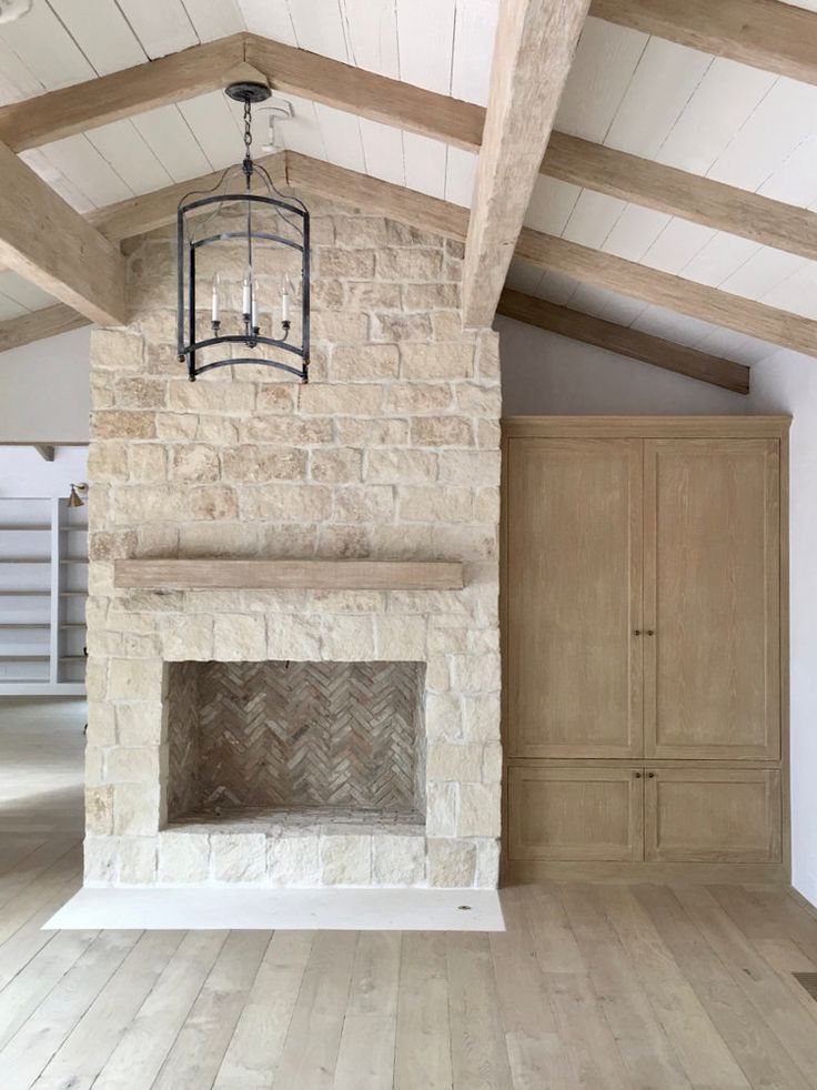 an empty living room with wood floors and exposed beams on the ceiling is lit by a hanging light fixture