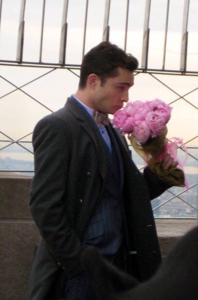 a man in a suit is holding flowers and looking down at the ground while another man looks on