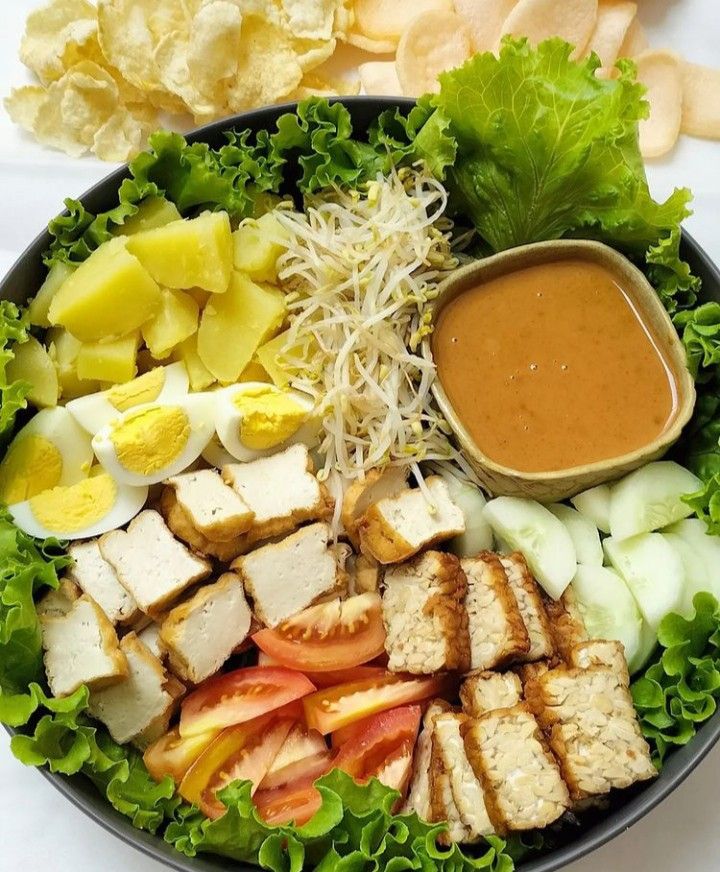 a salad with chicken, lettuce, tomatoes and other vegetables on the side