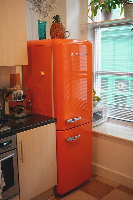 an orange refrigerator in a kitchen next to a window