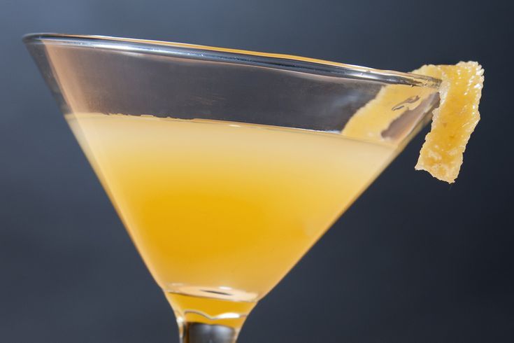 a close up of a martini glass with an orange peel on the rim and a black background