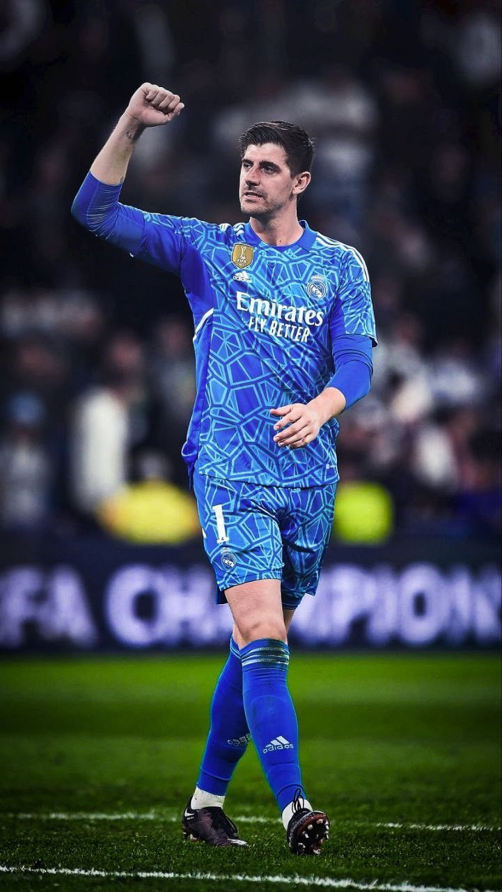 a man in blue uniform standing on top of a soccer field with his hand up