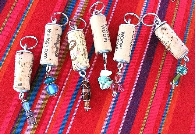 six wine corks with charms hanging from them on a red striped tablecloth background