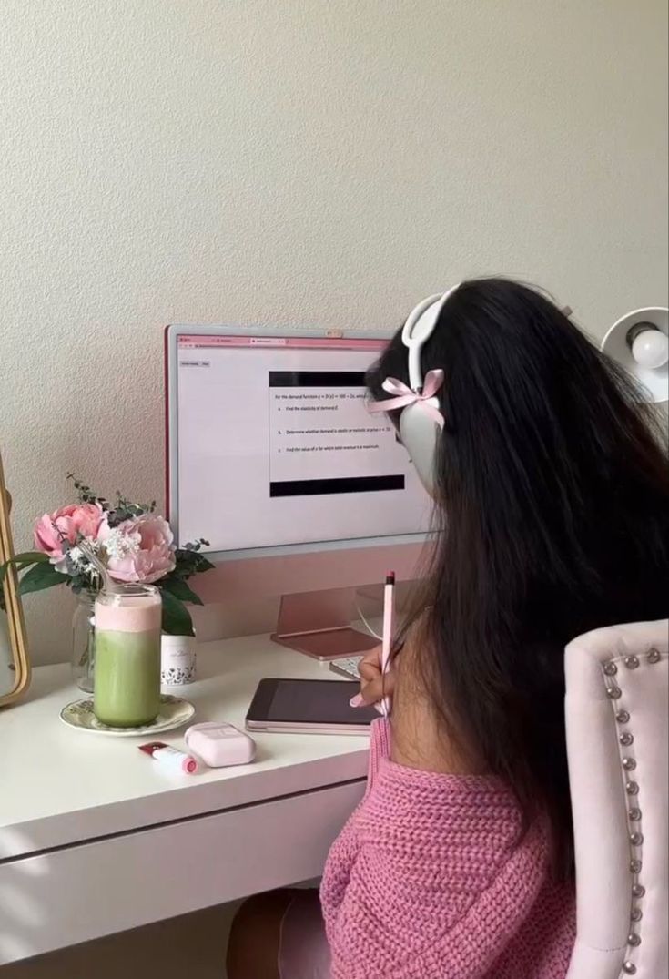 a woman sitting in front of a computer desk with headphones on her ears and holding a pencil