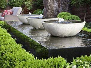 two large white bowls sitting on top of a water fountain in a garden area next to a tree