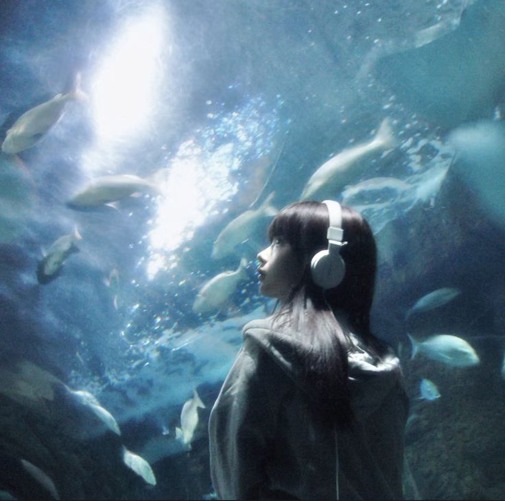 a woman with headphones standing in front of an aquarium filled with fish and looking up at the sky