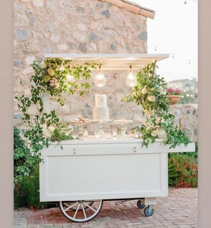 a white cart with flowers and greenery on the front is set up for a wedding reception