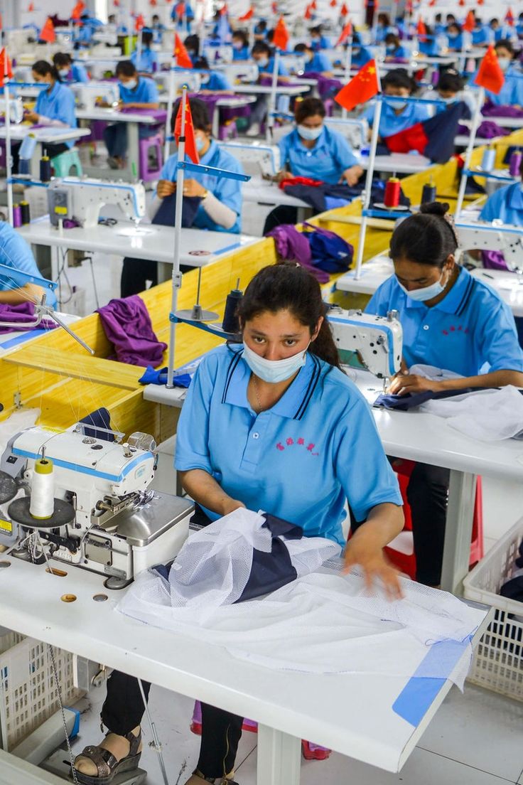 a woman is working in a factory with many sewing machines and people wearing masks on their faces