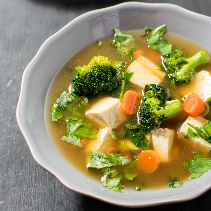 a bowl of soup with broccoli, carrots and tofu in it